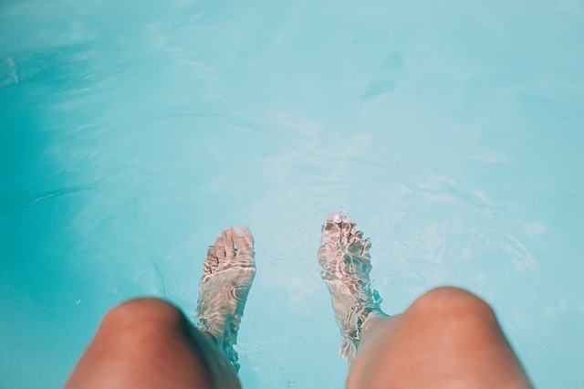 Žena má ponorené nohy v bazéne s modrou vodou
